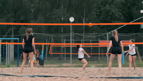 Four-girls-volleyball-players-play-on-the-beach-in-the-summer-participating-in-the-tournament-in-slow-motion-on-the-sand